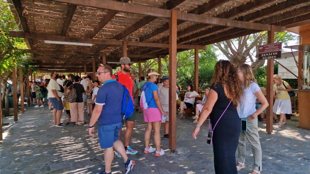 Palazzo di Cnosso: La Guida Vissuta Contro Caldo e Folla di Agosto 5 Gabriel vicino al cartello ufficiale 'Guida Turistica' a Cnosso, che mostra le guide disponibili e la tipica affluenza di Agosto all'ingresso.