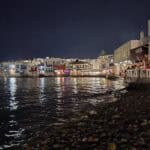 Vista notturna di Little Venice, Mykonos, con i riflessi colorati delle luci dei bar e ristoranti sull'acqua.