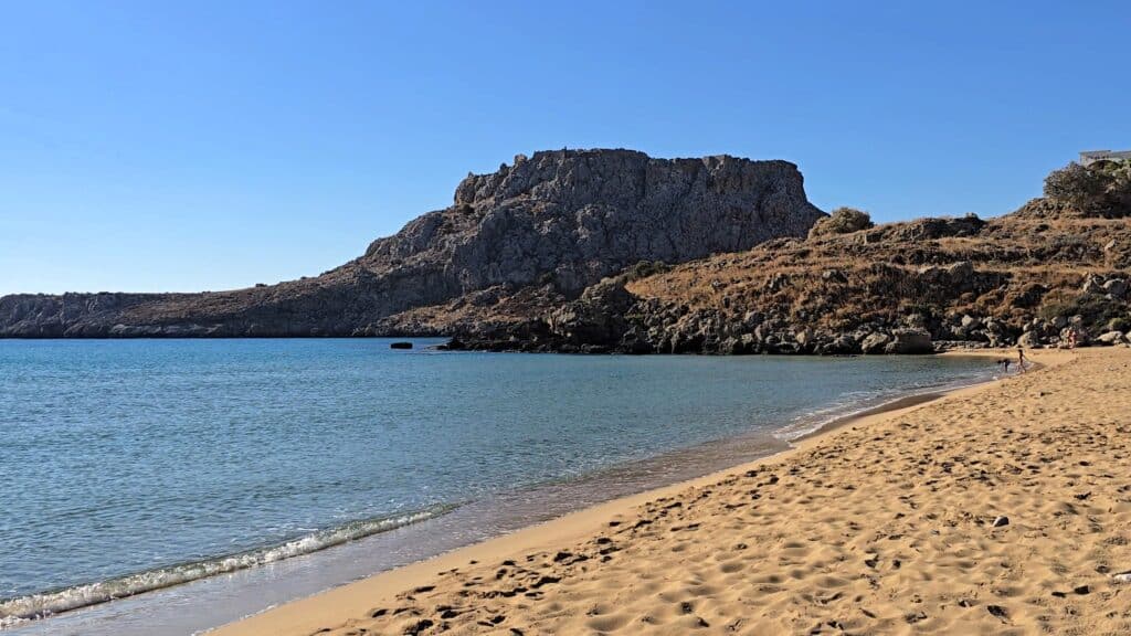 Scopri Agathi Beach (Spiaggia Sant'Agata): L'Essenza della "Sabbia Dorata" sull'Isola di Rodi 3 Vista mattutina della spiaggia Agathi Beach (Golden Sand) di Rodi, con la sabbia fine e le acque basse, incorniciata dall'imponente promontorio roccioso di Feraklos.