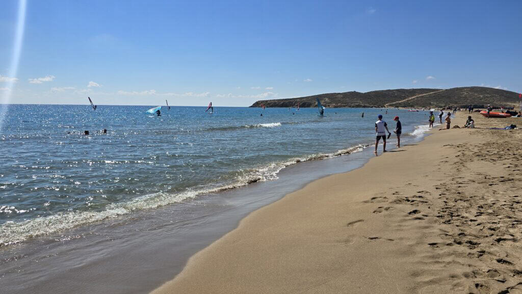 Spiaggia Prasonisi lato Mar Mediterraneo con onde tranquille, sabbia soffice e surfisti in lontananza.