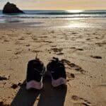 Scarpe da ginnastica sulla sabbia di una spiaggia dell'Algarve a Gennaio, con l'Oceano Atlantico e il sole basso all'orizzonte. L'immagine simboleggia la libertà di godersi la spiaggia, nonostante la temperatura fredda dell'acqua.