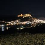 🌅 Lindos di Sera: Tra Acropoli Illuminata e Cene Romantiche sui Tetti di Rodi 1 Panorama notturno di Lindos Rodi con le case bianche illuminate e l'imponente Acropoli che brilla sulla sommità.