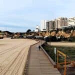 Vista aerea della spiaggia di Praia da Rocha a Portimão in Algarve a Gennaio, quasi completamente deserta e leggermente nuvolosa. Le due persone che passeggiano indossano tute e vestiti a maniche lunghe, evidenziando il clima invernale.