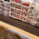 Close-up of a stall sign showing prices for "Lecca Lecca al Torrone" (Nougat Lollipops) at the Cremona Torrone Festival.