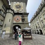 Ila, the article's author, waving in front of the Zytglogge (Clock Tower) in Bern, Switzerland, a key stop on the Green Train of the Alps route.