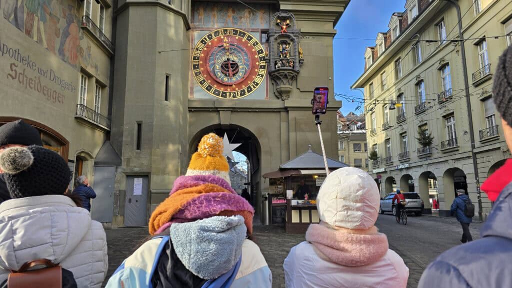 A group of warmly dressed travelers waiting below Bern's Zytglogge astronomical clock for the hourly figure show in winter.