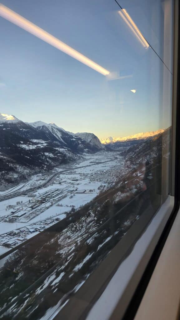 A spectacular winter view of a snowy alpine valley and mountains seen through the window of the Green Train of the Alps.