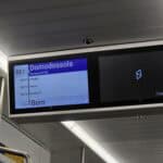 The Green Train digital display screen showing the itinerary from Domodossola to Bern, confirming the schedule and upcoming stops for easy navigation.
