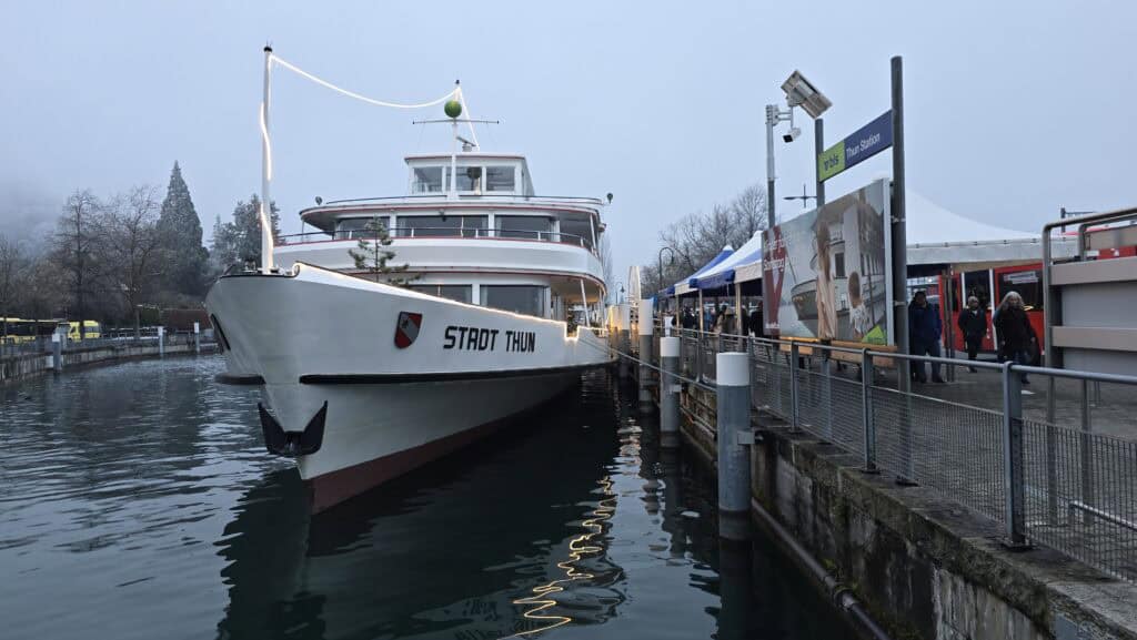 The 'Stadt Thun' boat docked at the BLS pier in Thun, showing the immediate proximity to the train station and the River Aare entry point.