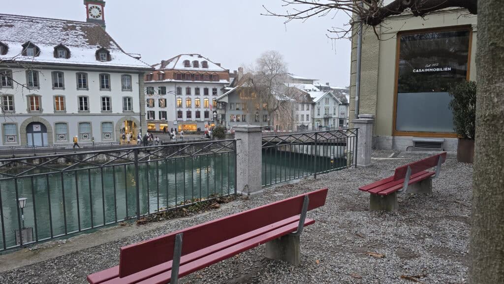 Thun's riverside promenade with red benches and snow, showing the beauty of the Old Town walk.