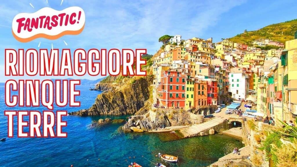 Colorful hillside village of Riomaggiore, Cinque Terre, Italy, overlooking a bright blue harbor with boats, sunny day.