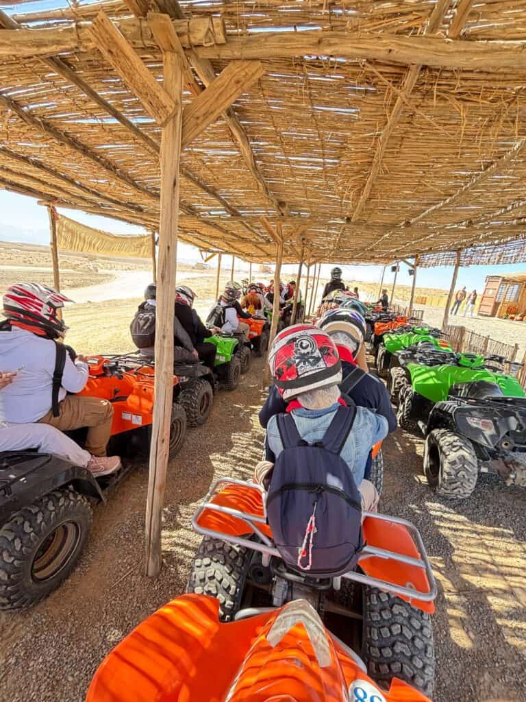 Marrakech Quad Biking: Thrills, Oasis Luxury & The City's Hidden Contrast 3 A long line of quad bikers, including Ila and Gabriel, queuing under a shaded canopy waiting to start the Marrakech desert tour.