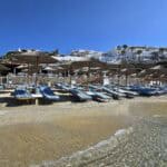 Panoramic view of the sunbeds and umbrellas at Cavo Psarou Mykonos, showing the quality and setup of the beach with the sea and the structural buildings in the background.