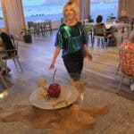 Elegant woman (Ila) in evening dress dining at a 5-star beachfront restaurant on Paralia Vlicha near Lindos, showcasing luxury dining options in Rhodes.