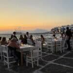 People dining at a restaurant along the Little Venice waterfront during a beautiful Mykonos sunset.
