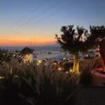 A breathtaking view of the Mykonos sunset from a hillside bar, featuring a lit-up heart sculpture and a classic windmill.