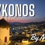 A panoramic view of the iconic Mykonos windmills and the town of Chora illuminated at night, with a beautiful blue twilight sky.