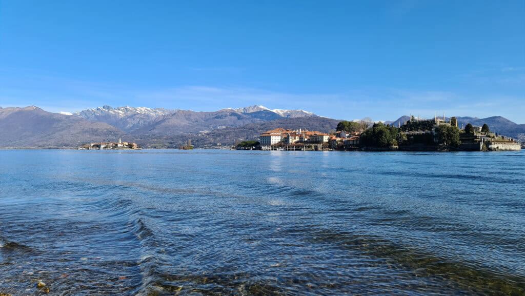 Wide panoramic view of the Borromean Islands (Isola Bella and Isola Pescatori) and the majestic snow-capped Alps mountains across Lake Maggiore in spring.