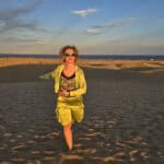 Woman wearing light clothes posing on the Maspalomas dunes in Gran Canaria in January at sunset.