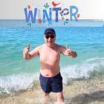 Man in swim shorts celebrating the warm water in Gran Canaria with a large 'WINTER' graphic.