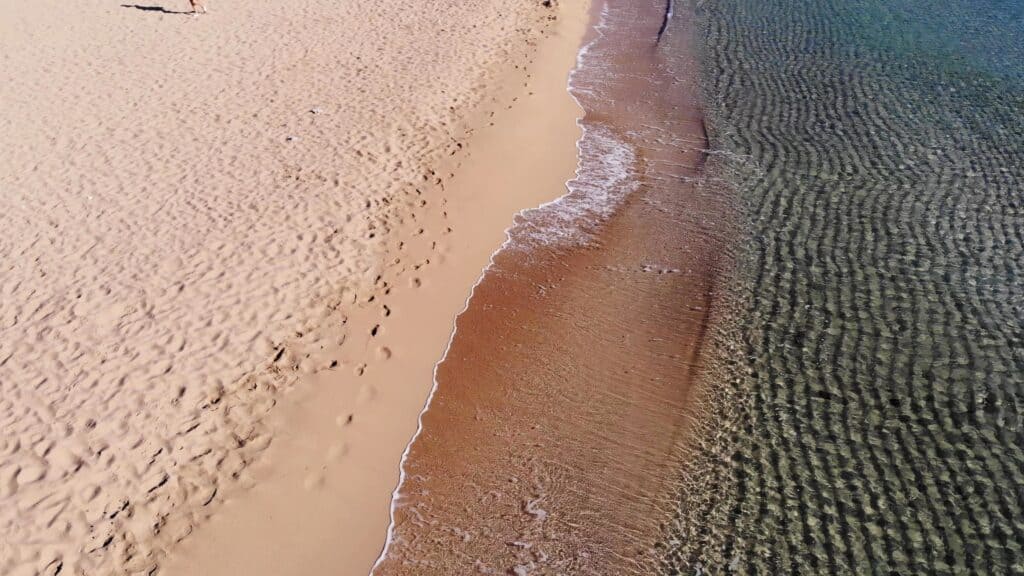 Agathi Beach Rhodes: The Essential Guide to the "Golden Sand" Gem 2 Detailed, high-angle shot highlighting the unique texture and color of the Golden Sand on Agathi Beach and the smooth transition into the shallow, crystal-clear water, emphasizing a peaceful beach day.