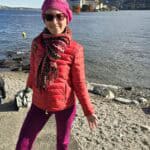 Author Ila smiling at the best Instagrammable spot on Isola Pescatori, with Isola Bella and the magnificent Borromeo Palace visible in the late autumn background (late October 2025).