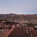 Wide panoramic view of Bergamo Alta's terracotta rooftops and the surrounding Orobie Pre-Alps, captured from the Campanone at sunset.
