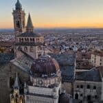 Aerial view of the Duomo and Basilica of Santa Maria Maggiore in Bergamo Alta, showing the illuminated monuments at sunset, as seen from the Civic Tower (Campanone).
