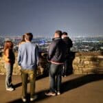 Travelers standing on the stone Venetian Walls of Città Alta, looking out at the glittering night panorama of Bergamo Bassa.