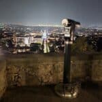 The telescope viewing tool on the Mura Venete or Campanone platform, offering a magnified look at the illuminated Bergamo Lower Town (Bassa) at night.