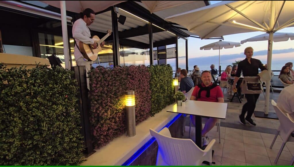 Tenerife Nightlife Expert Guide: How to Find Your Perfect Bar & The Canary Islands Vibe 7 Outdoor restaurant in Costa Adeje, Tenerife, with a man playing an acoustic guitar and a diner enjoying the evening atmosphere.