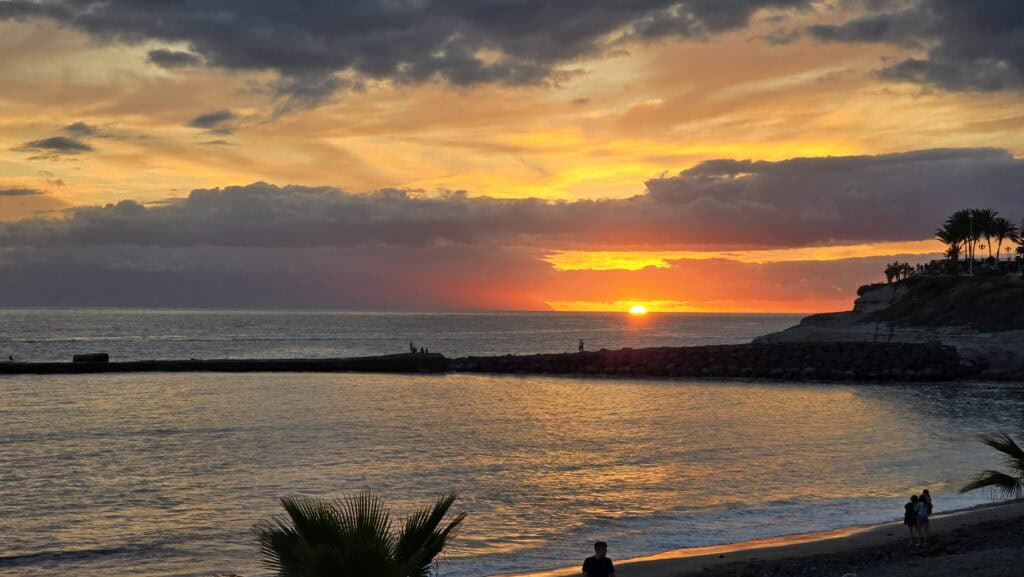 Tenerife Nightlife Expert Guide: How to Find Your Perfect Bar & The Canary Islands Vibe 6 Spectacular orange and purple sunset over the ocean in Costa Adeje, Tenerife, with a view of the beach and pier.
