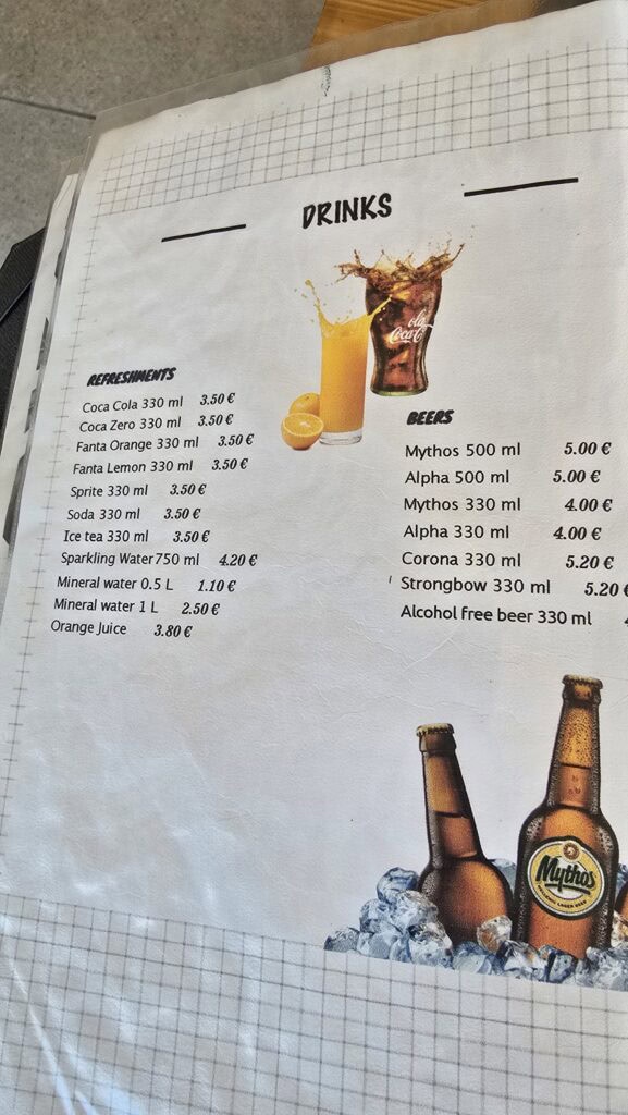 Photo of the Oasis Taverna Drinks Menu at Prasonisi Beach showing beer and soda prices.