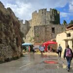 person walking umbrella wet promenade rhodes mandraki harbour walls