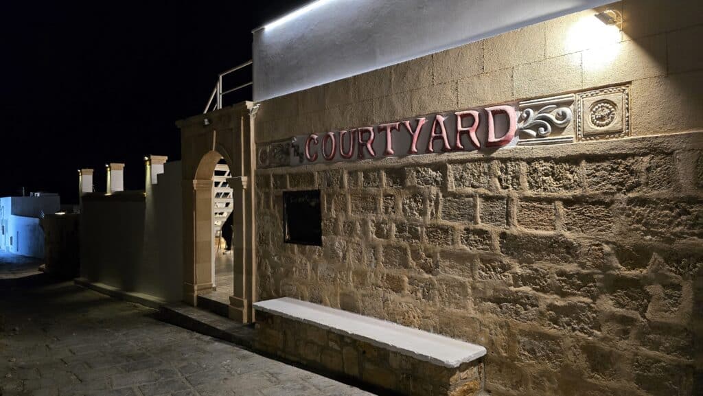 The striking, stone-walled entrance of CourtYard in Lindos at night, showing the access point to the popular elevated rooftop bar with Acropolis views.