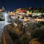 Panoramic night view of the entire illuminated historic center of Lindos, the main beach (Paralia Lindos), and the sea, seen from an elevated path near the Chapel of Saint George Pahimahiotis.