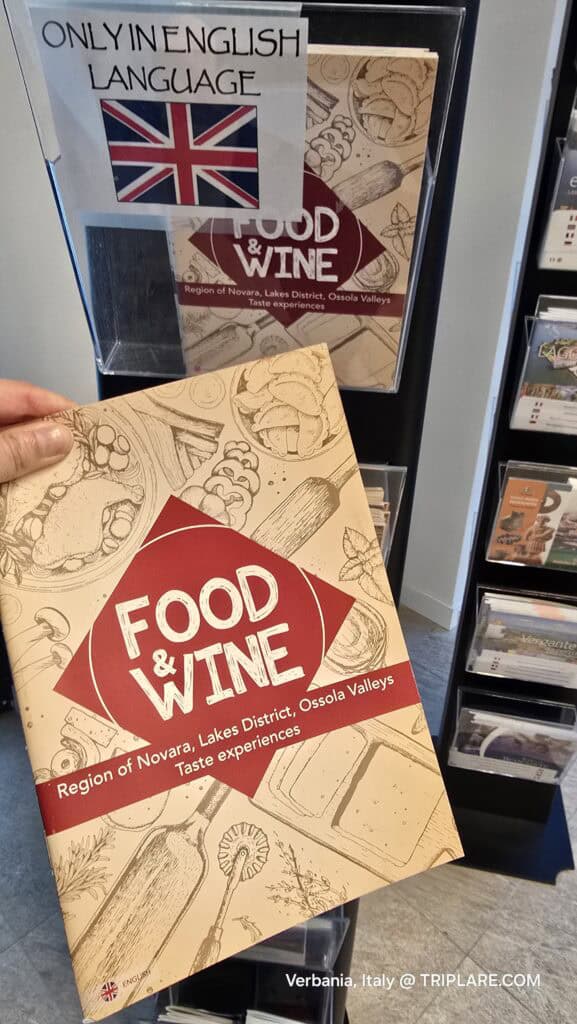 Author Ila's hand holding a Food & Wine brochure in English at the Verbania Tourist Office, showing local recipes.