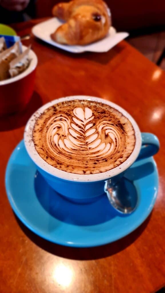 Close-up of a frothy cappuccino with a croissant (brioche) blurred in the background, typical Italian breakfast in Crema