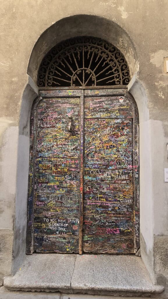 Historic wooden doorway in Crema near Piazza Duomo, covered in tourist graffiti, famous from the film Call Me By Your Name