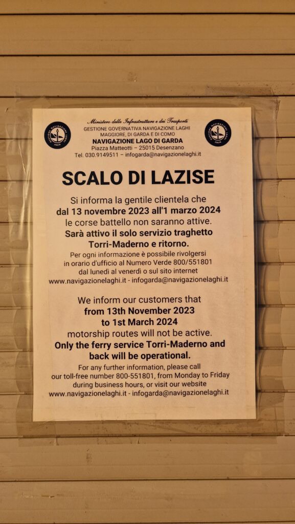 A photo of a posted ferry schedule board showing that the Lake Garda general line service (battelli) is suspended during the winter months, confirming limited lake transportation.