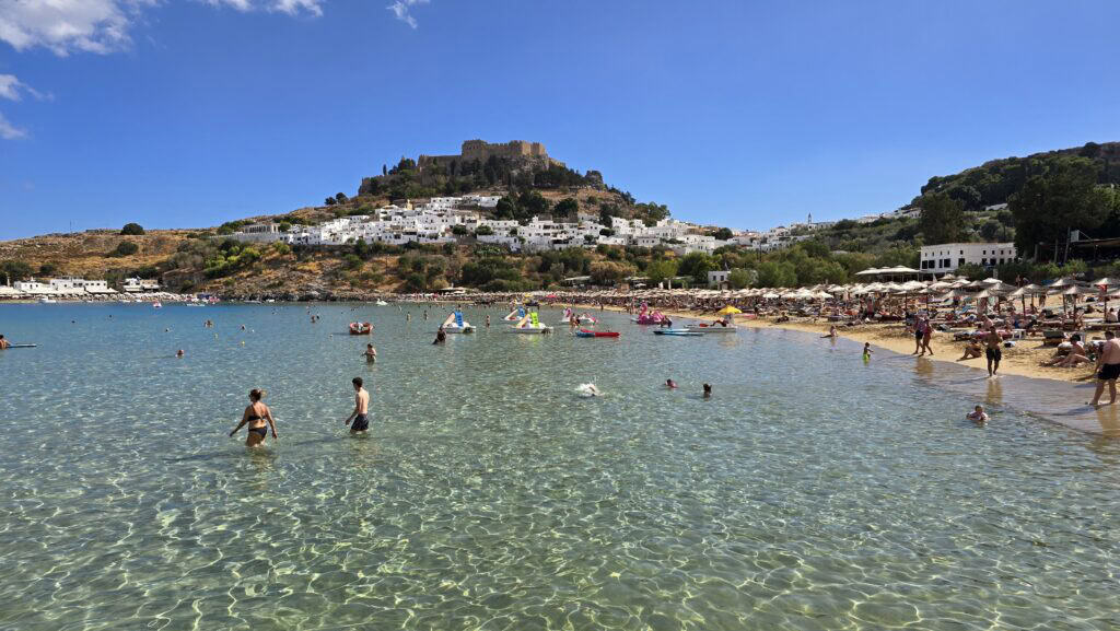 People swimming at Lindos Beach, Rhodes, with the Acropolis in the background, in early October.