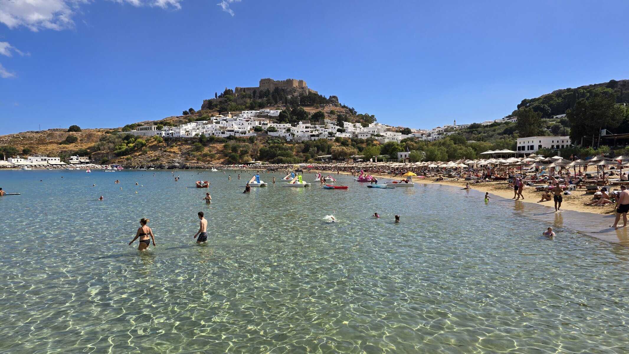 People swimming at Lindos Beach, Rhodes, with the Acropolis in the background, in early October.
