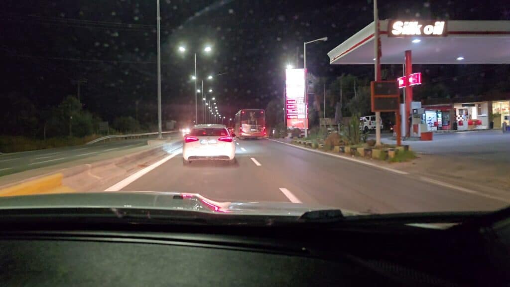 Night view from car on the main coastal road from Lindos to Rhodes, showing illuminated, double-lane highway, a gas station, and a moving bus.