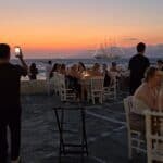 Little Venice Mykonos at sunset showing the crowded seaside restaurants on the square, offering a pleasant dining experience with a view.