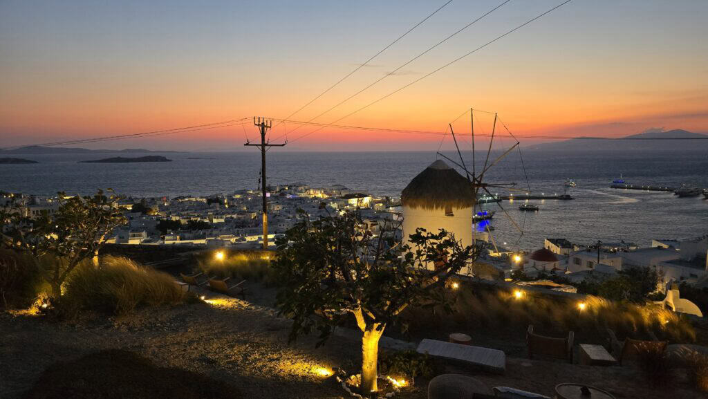 The exclusive atmosphere of Numi Sunset Bar in Mykonos, showing chic tables, cocktails, and the beautiful sea view at dusk.