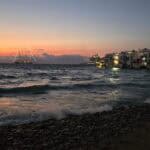 Mykonos sunset from a free viewpoint near Little Venice, showing the beach and romantic silhouette of the houses. Little Venice beach showing the iconic houses and a large, illuminated cruise ship docked nearby.