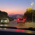 Mykonos sunset view captured from a car window or roadside stop, showing the illuminated cruise ships and the sea horizon.