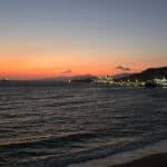 Sunset in Mykonos Town from the road past the port, with a cruise ship sailing in the Aegean Sea.