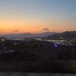Vibrant sunset over the sea with a view of the road and surrounding hills, highlighting the casual beauty of Mykonos sunsets, visible even while driving.