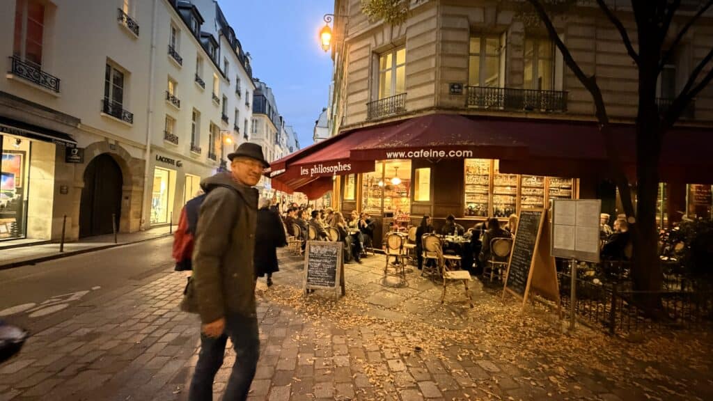 Parisian street scene with a corner café and a person walking in the late afternoon autumn light.